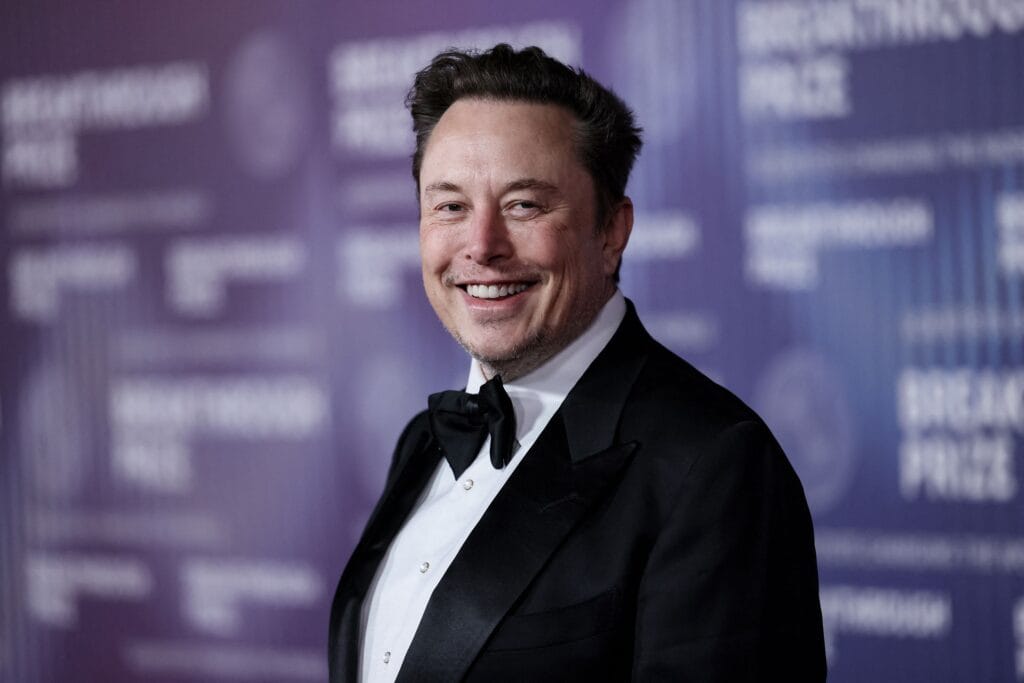 A clear, high-resolution portrait photo of Elon Musk, the entrepreneur and CEO of Tesla and SpaceX, wearing a dark jacket and white shirt, looking directly at the camera with a slight smile
